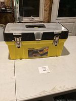 Yellow and black Stanley 19-inch tool box closed, showing metal latches and clear top with organizer tray inside.