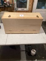 Closed wooden tool chest on table, showing latches and light wood finish.