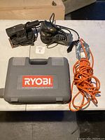 Ryobi kit case, Black & Decker finishing sander and orange corded work light arranged on table.