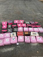 Overview of 36 pairs of women's dress shoes in original boxes, arranged on pavement. Boxes mainly pink with some black, purple and patterned designs.