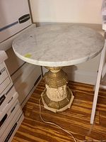 Round marble end table showing white marble top with veining and a decorative sculpted gold and cream base with hexagonal marble foot.