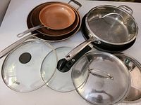 Overview of assorted frying pans and pot lids showing pans stacked and various lids