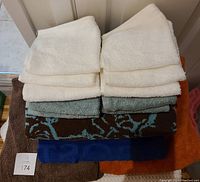 Image showing neatly folded assorted bath towels and washcloths in white, cream, blue, brown, orange and patterned colors stacked on each other.