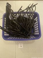 Top view of basket holding multiple black metal swirl and flat style wall mount brackets stacked inside.