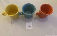 Top view of three colorful Fiesta mugs in yellow, blue, and orange arranged side by side showing interior and handles.