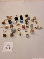 Photo showing a collection of 31 costume jewelry pieces including rings of various sizes, styles and colors, along with several brooches such as pearl cluster and animal shapes.