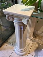 Off-white Greek style pedestal with fluted column and Ionic capital, showing glossy finish and square flat top surface.