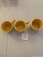 Overhead view of three yellow Fiesta mugs with handles aligned.