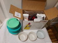 Photo of KitchenAid hand mixer in box, three turquoise food storage containers with lids, two small white bowls, and instruction manual