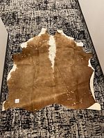 Full view of the brown and white cowhide rug laid flat showing shape and discoloration spots.