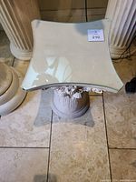 Top-down photo showing the curved square glass top of the pedestal with reflective surface.