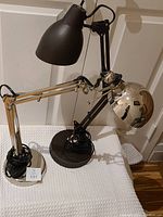 Photo showing two adjustable desk lamps with different styles and finishes placed together.