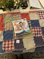 Patchwork quilt laid out with the new packaged waterproof mattress cover placed on top. Quilt shows various colorful fabric squares in diverse patterns and colors.