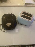 Photo shows black Gotham waffle maker and powder blue Keenstone toaster on a table.
