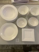 Photo showing various white dishes including soup bowls, small bowls, flat dinner plates, and a square plate all arranged on a table.