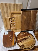Photo showing five wooden cutting and cheese boards in assorted sizes and styles, some with attached cheese knives and forks, all well used.