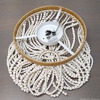Top view of the chandelier showing white metal frame, three light sockets, and circular wood bead strands attached in layers.