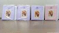 Four mini photo albums in pastel colors, two lavender, one light purple, and one light pink, each shrink-wrapped and with a windowed front cover showing a photo insertion.