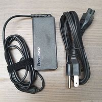 Front view of Lenovo AC/DC adapter with attached cable and power cord laid out beside it on wooden surface.