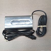 Full view of metallic Alienware AC adapter with two cables coiled beside it on a flat surface.