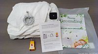 Complete lot showing the folded white conductive grounding sheet, grounding cord, yellow grounding tester plug, and informational booklet