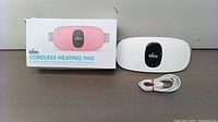 White idoo cordless heating pad with black control panel on table with USB charging cable and box beside it