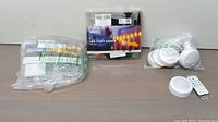 Two boxed LED fairy light sets and six white round RGB circle lights with remote controls wrapped in plastic packaging on a table.