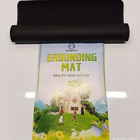 Black grounding mat partially unrolled, showing colorful printed insert with 'Panbmao Grounding Mat Health from Nature' text and natural scene graphic.