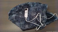 Folded gray plush 50 x 60 heated blanket with white remote control on top, showing controller with buttons and display.