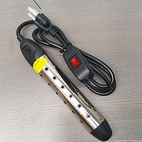 Full view of the stainless steel submersible bucket heater showing star-shaped cutouts, black end caps, and attached power cord with inline switch.