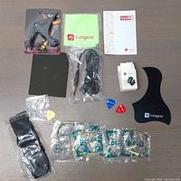 Overview of all items included in the Vangoa accessory kit, showing guitar strap, capo, guitar picks in packaging, string winder, cleaning cloth, owner's manuals, multiple sets of guitar strings, and pick holder.