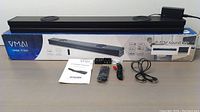 Main sound bar and subwoofer on box, remote, cables, user manual displayed on table.