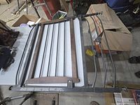 Metal baby gate with wood top rail and vertical metal bars, latch mechanism, and mounting hardware visible.