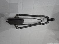 Boat motor flusher with two hoses and nozzle attachment shown on a tiled white wall background.