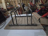 Metal bicycle rack with four upright supports on a metal base, designed to hold two bicycles.