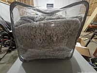 Queen size comforter stored in zippered clear plastic bag, appears thick and plush with grey tones.