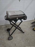 Photo of portable Cuisinart grill barbecue with foldable stand and wheels in a garage setting.