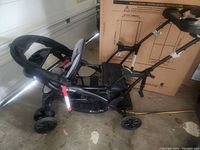 Side view of black and gray double stroller with rear stand and seat option in garage setting