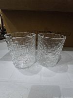 Close-up of two textured glass candle holders showing the woven-like pattern on clear glass.