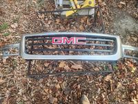 Rectangular GMC grill shown laying on the ground, surrounded by leaves and a metal frame underneath