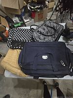 Top view of five bags: large blue bag, two black carry bags, and two patterned hand bags (polka dot and black/white pattern)