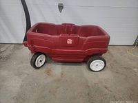 Side view of red double seat kids wagon with four white wheels and black handle.