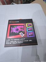 Box of Blackweb LED TV mood light with remote control shown on a white grid surface.