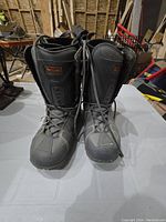 Front view of the pair of grey men's size 12 snowboarding boots standing upright on a white surface.