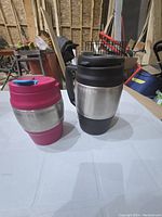 Pair of Bubba insulated travel mugs on a white table in a workshop/unfinished room, showing front and side views.