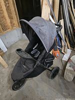 Black single seat jogging stroller with canopy, three wheels, and small scuff marks on front section in a workshop setting.