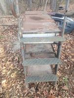 Close-up of steel ladder side steps with diamond plate pattern, exhibiting rust and wear.
