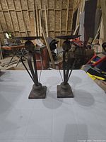 Photo showing two steel candle holders with a rustic, industrial look on a workbench in a cluttered workshop.