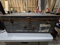 Front view of the large heavy-duty metal chest showing handles, latches, and military stencils with wear and rust.