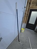 Full view of the hockey stick leaning against a garage door, showing taped handle and curved blade.